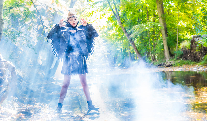 Photograph of teen girl dressed as a Black Angel in the woods by a creek with Smoke