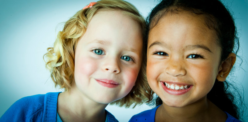 Photograph of a caucasian girl and black girl smiling on a seamless background