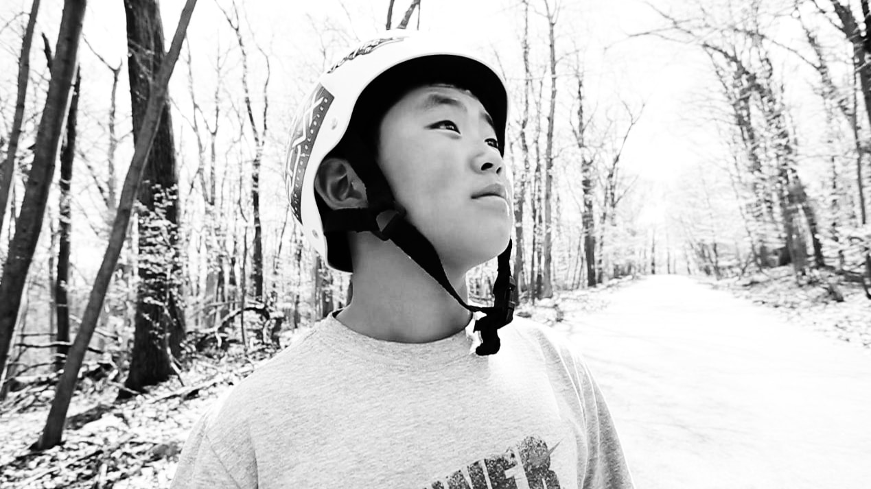 Photograph of Asian Boy long boarding in wooded area