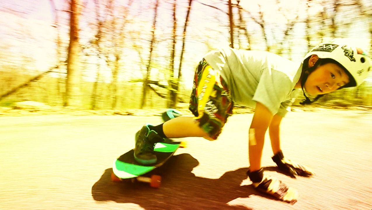 Photograph of Asian Boy long boarding in wooded area