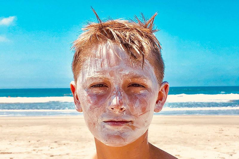 Photograph of a caucasian teenage boy with face covered with sunscreen at beach