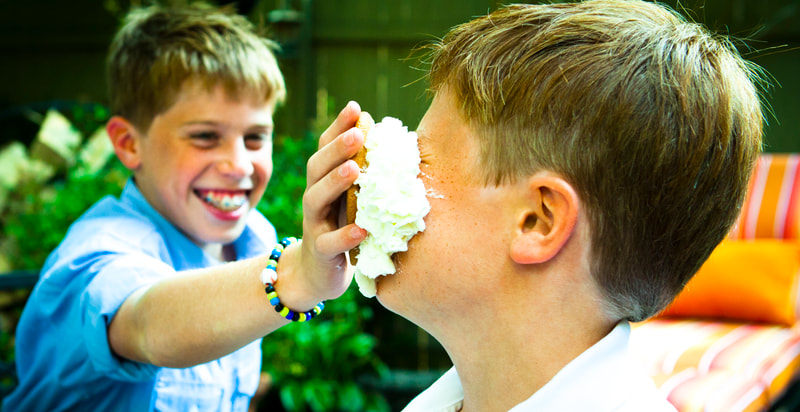 Photograph of a boy shoving a cream pie in brothers face