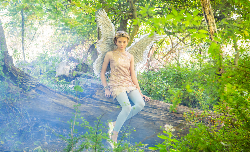 Photograph of teen girl dressed as an Angel in the woods sitting on a tree stump with Smoke