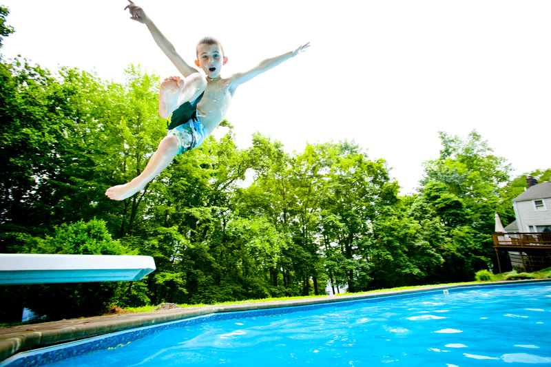 Photograph of Boy in swimsuit jumping off pool diving board