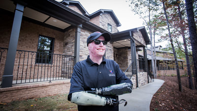 Photo of wounded combat veteran Michael Schlitz in front of his new smart home provided by the Gary Sinise Foundation